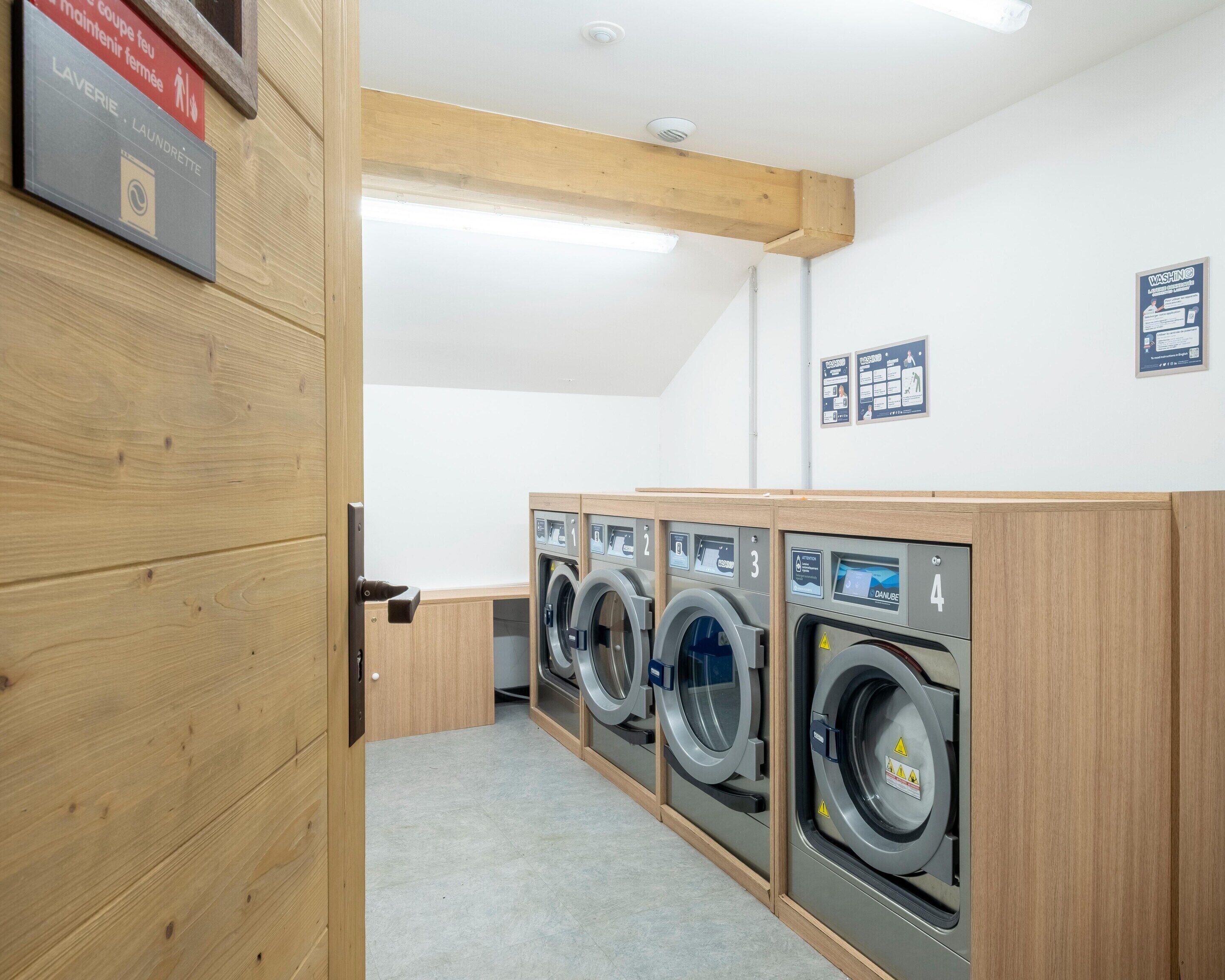 A laundry facility with four washing machines, wooden paneling, and informational signs on the walls.