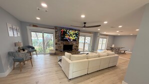 A spacious living room with a stone fireplace, a large flat-screen TV, a ceiling fan, and a dining area with a table and chairs. - Modern Lakefront Getaway ,Family Friendly & Relaxing (Keystone Heights)