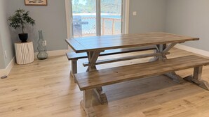 A wooden table with benches in a room with light gray walls and a view through a glass door. - Modern Lakefront Getaway ,Family Friendly & Relaxing (Keystone Heights)