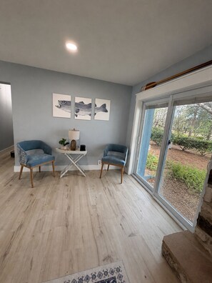 A modern living room with two blue armchairs, a small table with a lamp, and artwork on the wall.