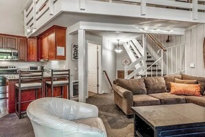 Eine moderne Küche mit Holzausstattung, ein Essbereich mit einem weißen Stuhl, ein braunes Sofa und eine Treppe.