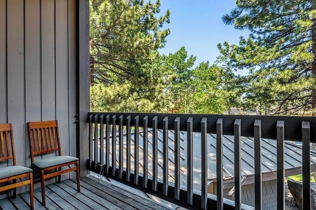A wooden deck with two chairs, a metal railing, and a view of trees and a building.