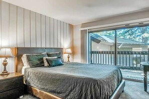 Ein Schlafzimmer mit einem großen Bett, zwei Nachttischen mit Lampen, einer Schiebetür zum Balkon und Blick ins Freie.