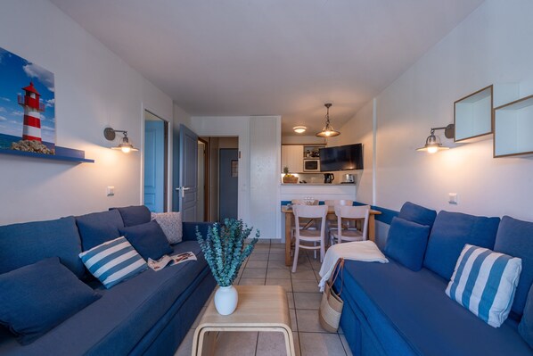 A living room with a sofa, a coffee table, and a dining area with chairs and a table. - Cozy Stay by the Shops (Fort-Mahon-Plage)