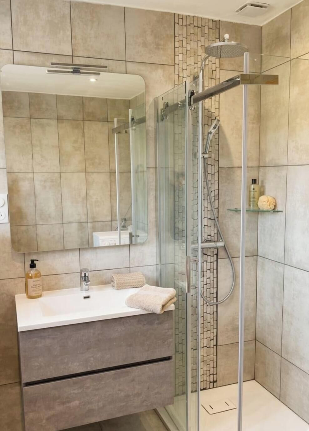 Une salle de bain moderne avec une douche à parois de verre, un meuble-lavabo avec un miroir et une serviette.