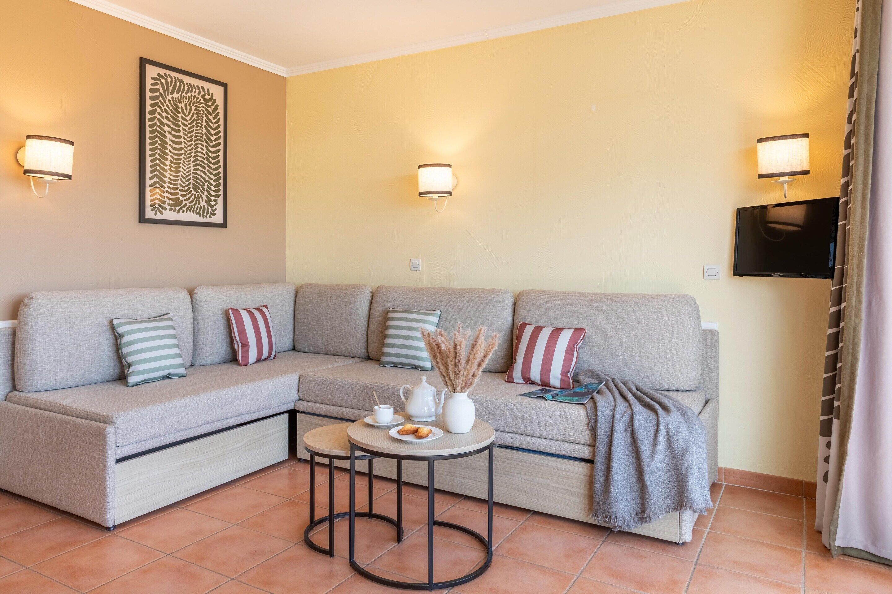 Sala de estar com sofá modular, mesa redonda pequena com bule e xícaras, e luminárias fixadas na parede.