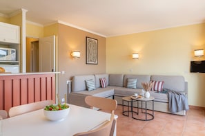 Una sala de estar con sofá, una mesa de comedor con sillas, una zona de cocina con microondas y un televisor montado en la pared.