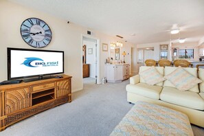 Ein Wohnzimmer mit Fernseher, einer Uhr, einem Sofa und einer Küche im Hintergrund.