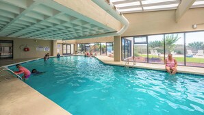 Ein Innenpool mit großen Glaswänden, einer Decke mit Gitterstruktur und Blick ins Freie.