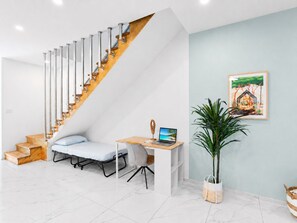 Un interior moderno con una escalera, una cama, un escritorio con una computadora portátil y una planta en maceta.