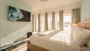 A bedroom with a large bed, a painting on the wall, and a view through the window.