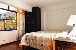 Ein Schlafzimmer mit Bett, Nachttisch, Lampe, Kleiderschrank und einem Fenster mit Vorhängen.