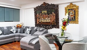 Ein Wohnzimmer mit einem Ecksofa, einem Glastisch und zwei gerahmten Kunstwerken an der Wand.