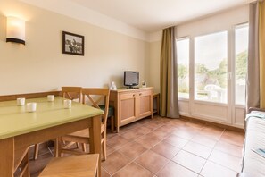 Quarto com mesa de jantar, cadeiras, televisão e janela com cortinas.