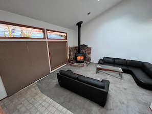 Ein Wohnzimmer mit Kamin aus Stein, schwarzen Ledersofas und Blick durch ein Fenster mit Buntglasdekor.
