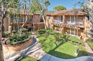 A courtyard with a central pathway, surrounded by neatly trimmed hedges and trees. - Spacious, 2-bedroom condo with full kitchen, AC, Wifi, gym, pools and hot tub. (Anaheim)