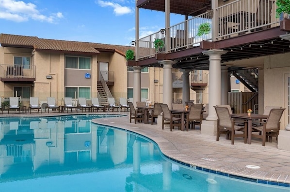 A hotel with a swimming pool, outdoor seating, and a covered area with stairs.