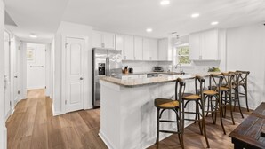 Una cocina moderna con armarios blancos, una isla central con taburetes de bar y un refrigerador de acero inoxidable.