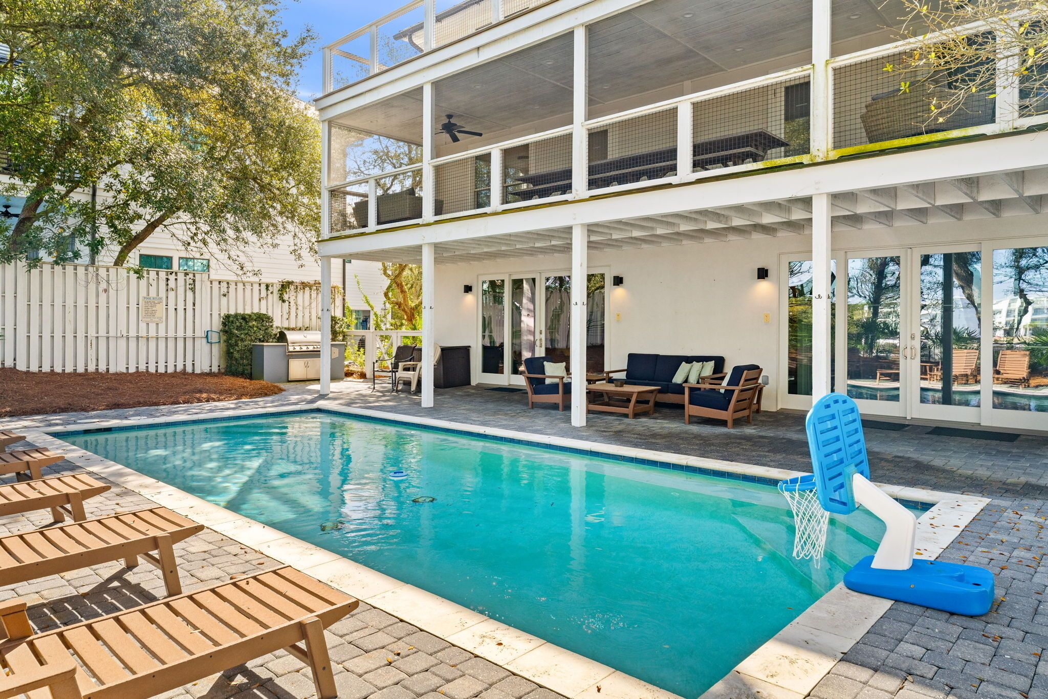 A pool area with lounge chairs, a basketball hoop, and a multi-level building with outdoor seating.