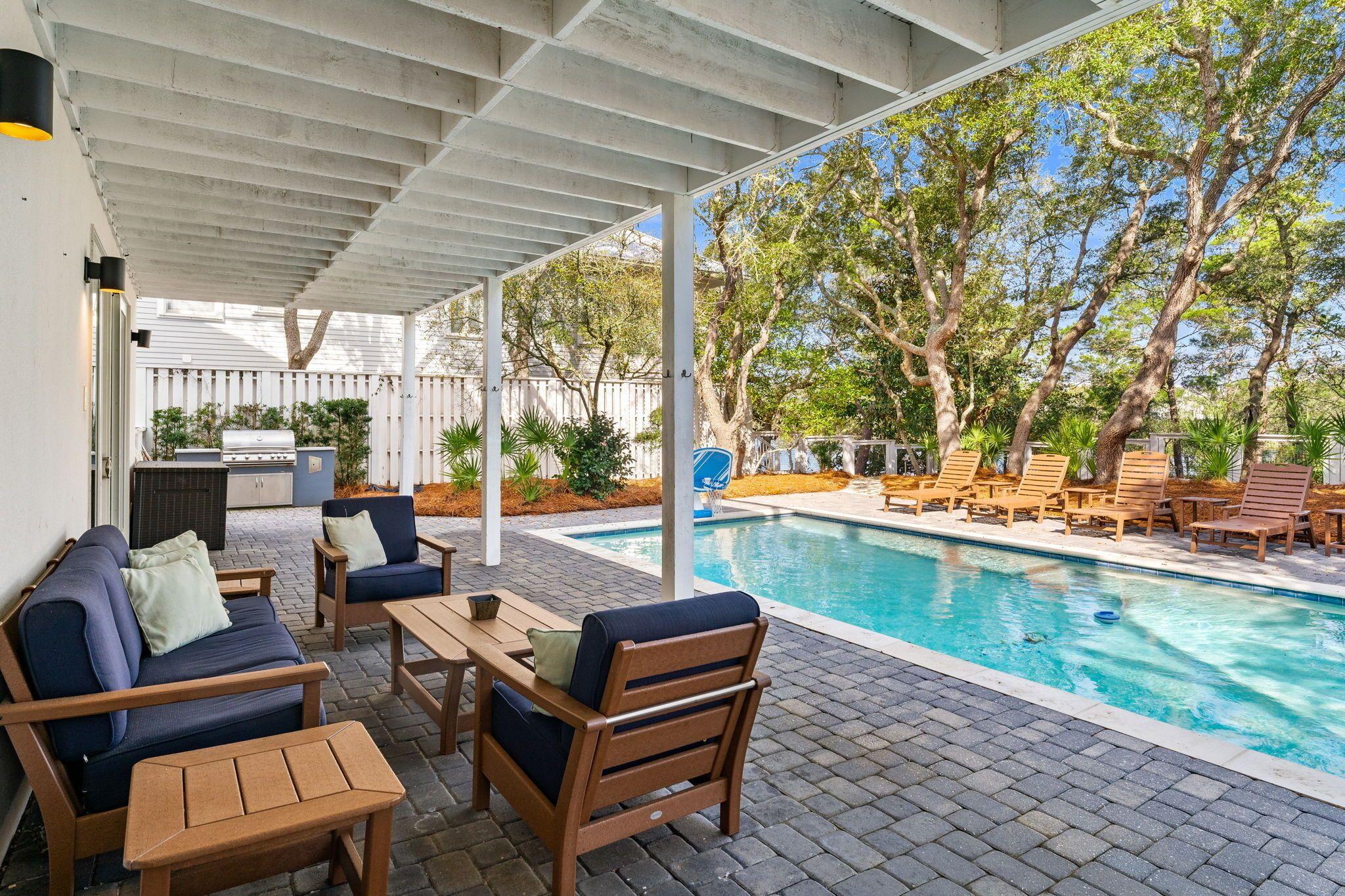A covered outdoor area with a pool, lounge chairs, and a barbecue grill.