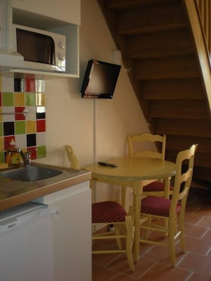 A kitchen with a microwave, a sink, a small refrigerator, and a dining table with chairs. - Courtinn Aqua (Avignon)