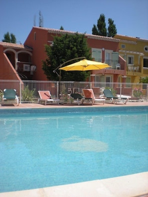 A swimming pool with lounge chairs and an umbrella, surrounded by a white fence. - Courtinn Aqua (Avignon)