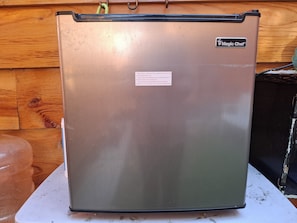A stainless steel refrigerator with a 'Magic Chef' label, placed on a white surface against a wooden wall.