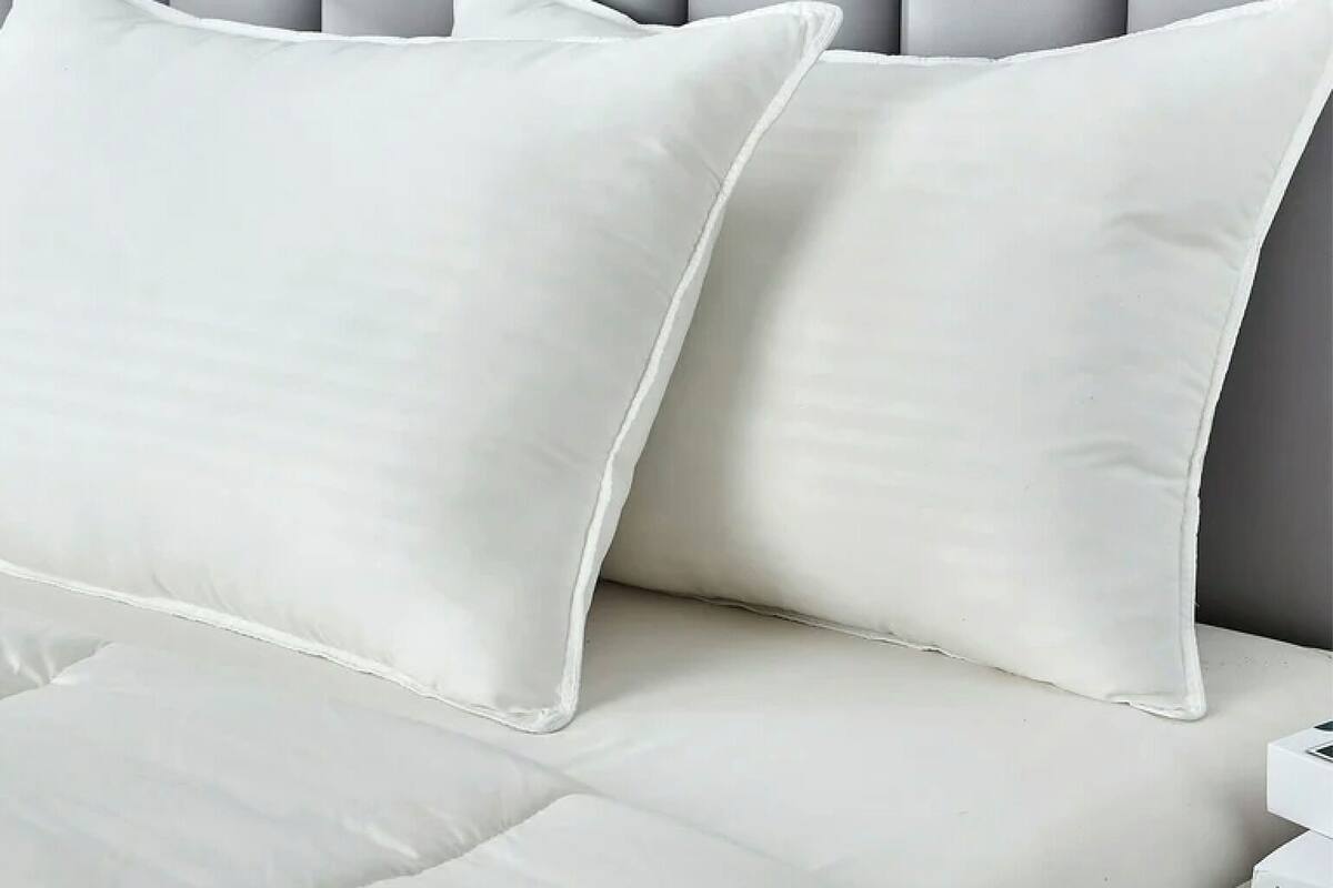 Cama com roupa de cama e almofadas brancas, cabeceira estofada cinza e mesa de cabeceira branca.