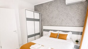 Un dormitorio moderno con una cama, un armario, un equipo de aire acondicionado y una pequeña planta en la mesita de noche.