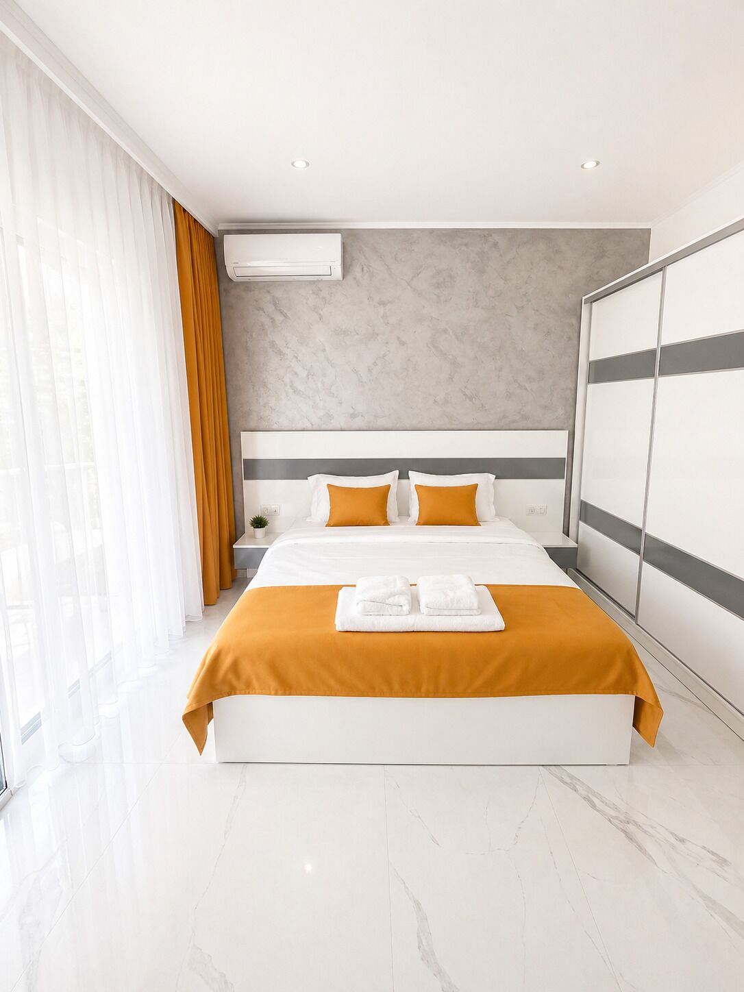 Camera d'albergo moderna con un letto grande, pavimento in marmo e un'ampia finestra con tende.