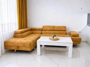 A modern living room with a sectional sofa, a white coffee table, and a decorative tray. - Pami Apartments (Nea Peramos)
