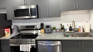 A modern kitchen with stainless steel appliances, grey cabinets, and a tiled backsplash. - New 1BR Suite in Aspen Ridge, Saskatoon for a home away from home experience. (Saskatoon)