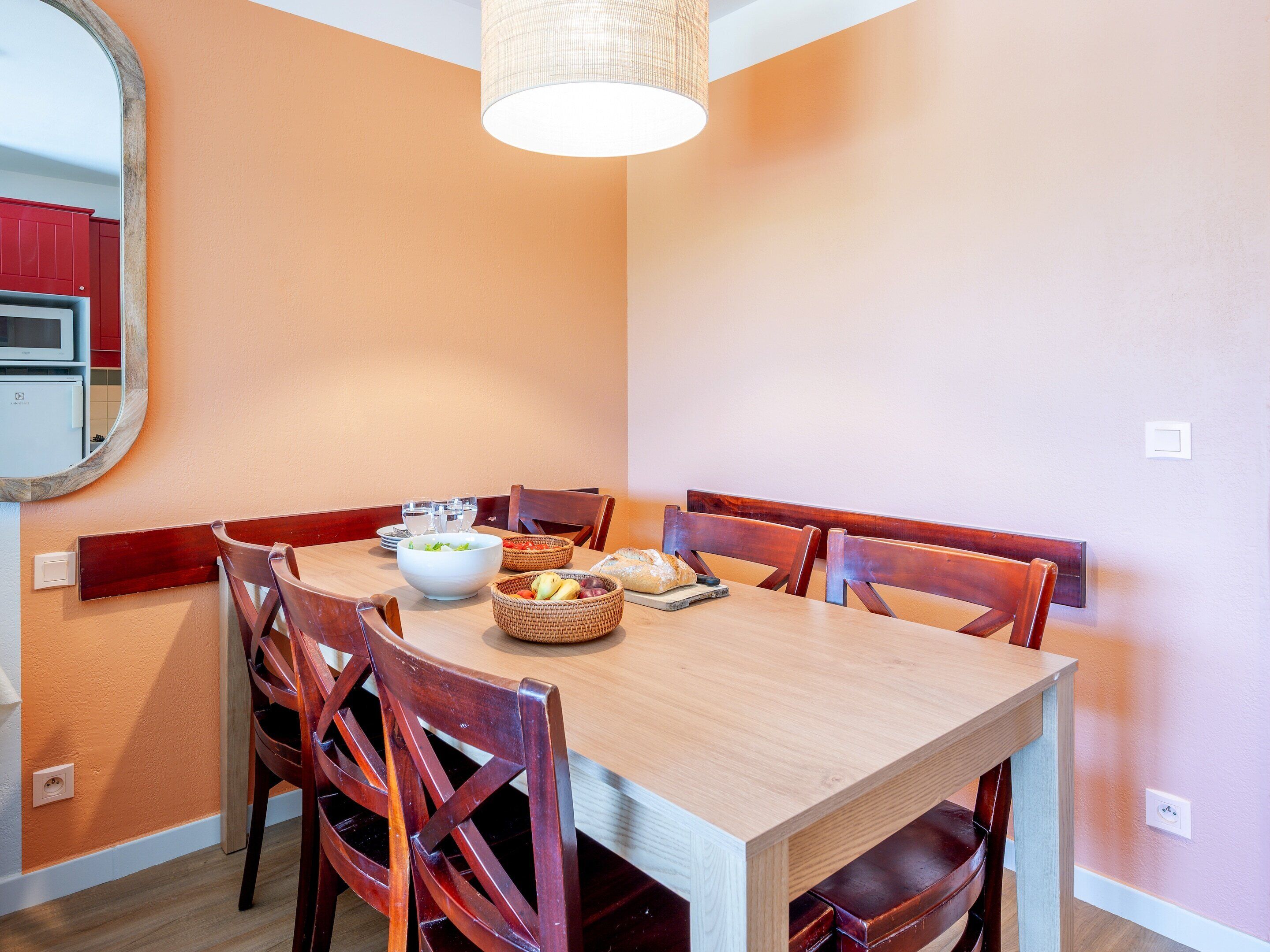 A dining area with a wooden table, six chairs, a hanging light fixture, and a wall-mounted mirror.