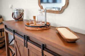 Un comptoir de bar en bois, avec un plateau où sont posés des verres et une bouteille, un miroir au-dessus et un meuble en bois en dessous.