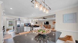 Een moderne keuken met een groot eiland, roestvrijstalen apparatuur en een eethoek met een opvallend houten middelpunt.