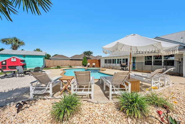 A pool area with lounge chairs, a wooden deck, and a building with a red exterior.