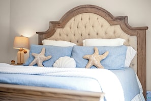 Un lit avec une tête de lit capitonnée, deux oreillers, une lampe et des décorations en forme d’étoiles de mer.