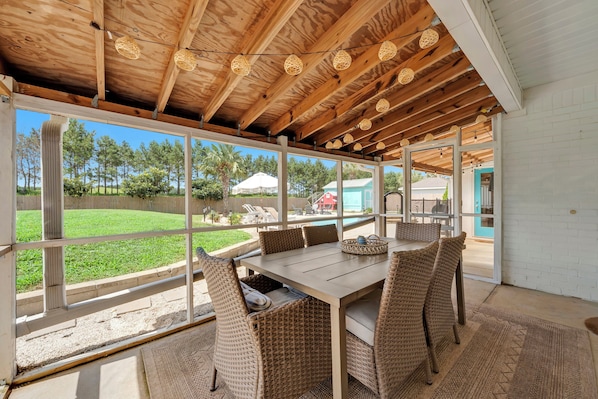 A covered patio with a table and wicker chairs, large windows, and a wooden ceiling.