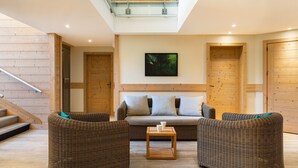 A modern living room with a sofa, two armchairs, a coffee table, wooden walls, a staircase, and a framed picture on the wall. - Apartment Near Ski Resort (Araches-la-Frasse)