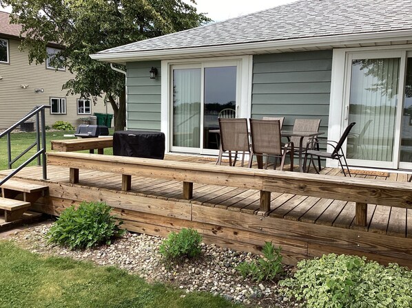 A deck with outdoor furniture, a barbecue grill, and a house with large windows.