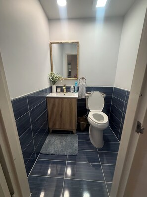 Ein Badezimmer mit Toilette, Waschbecken, Spiegel und gefliesten Wänden.