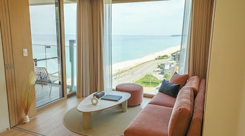 Una sala moderna con un ventanal que da a una playa, un sofá, una mesita y una silla.