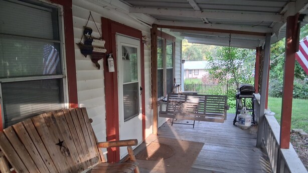 A wooden porch with a bench, a grill, and a patio table. - Cabin 1 at the Lake, at Monterey Park an boat launch area (Zavalla)