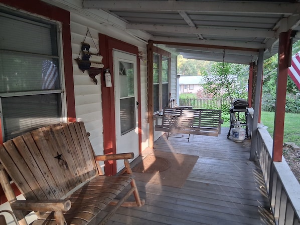 A wooden porch with a bench, a grill, and a patio table.