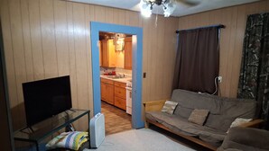 A living room with a television, sofa, and a kitchen visible through an open doorway. - Cabin 1 at the Lake, at Monterey Park an boat launch area (Zavalla)