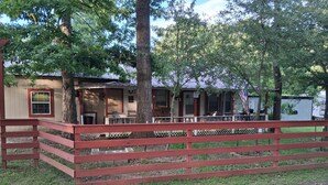 A rustic cabin with a porch, surrounded by trees and a wooden fence. - Cabin 1 at the Lake, at Monterey Park an boat launch area (Zavalla)