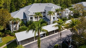 A multi-story hotel with a flat roof, surrounded by palm trees and a forested area. - Live the Naples Lifestyle.. Resort Amenities & Coastal Charm (Naples)