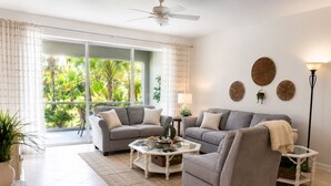 A living room with two grey sofas, a glass coffee table, and a floor lamp. - Live the Naples Lifestyle.. Resort Amenities & Coastal Charm (Naples)