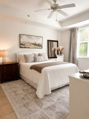 Ein Schlafzimmer mit Bett, Nachttisch, Fenster mit Vorhängen und einem Wandbild.