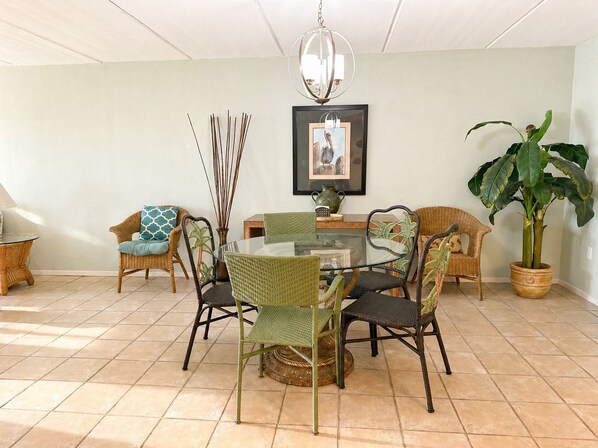 A dining area with a glass table surrounded by wicker chairs, a chandelier, and a framed picture on the wall. - High-Floor Saida Beachfront - Pool + Ocean View (South Padre Island)